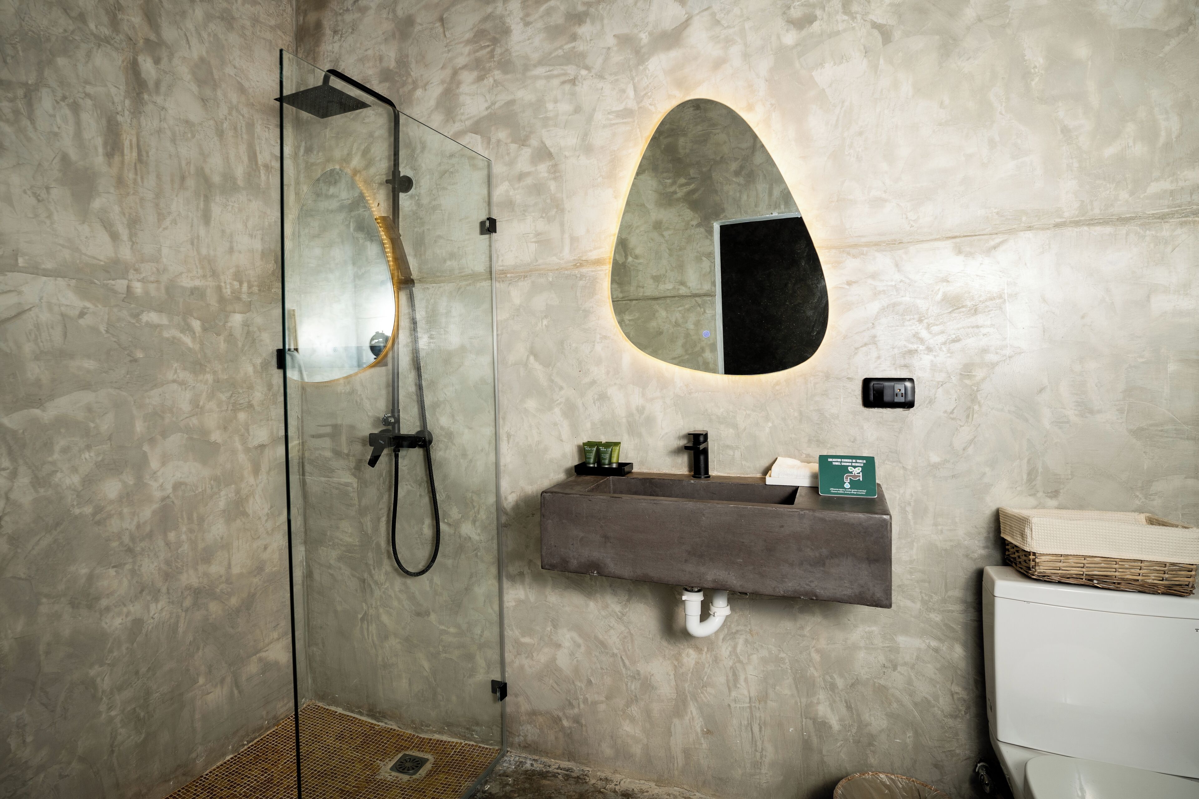 Une salle de bain moderne dotée d’une douche à parois de verre, d’un lavabo intégré avec un plan de travail en pierre et d’un grand miroir à la forme originale.