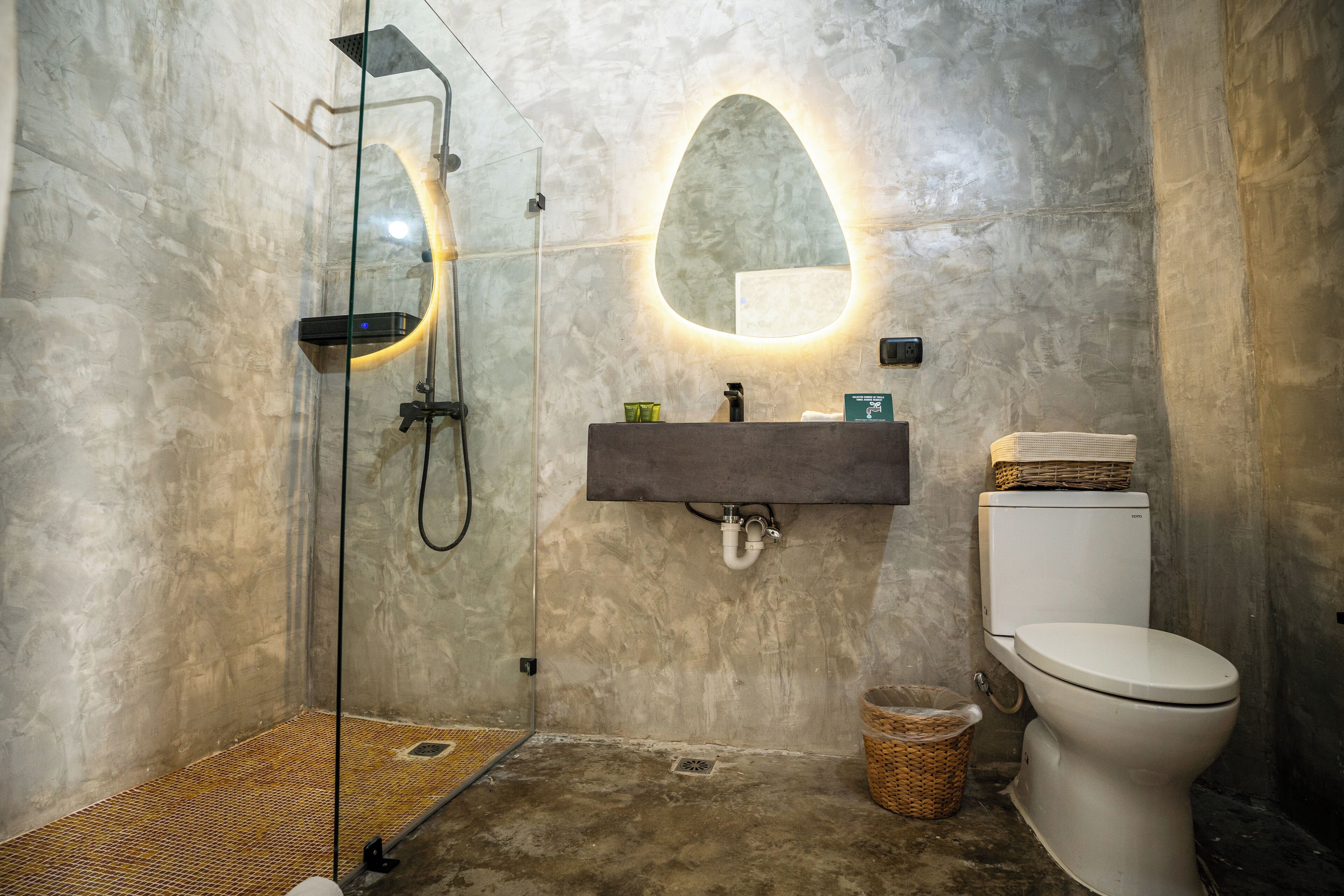 Une salle de bain avec une douche à parois de verre, un lavabo fixé au mur et des toilettes.