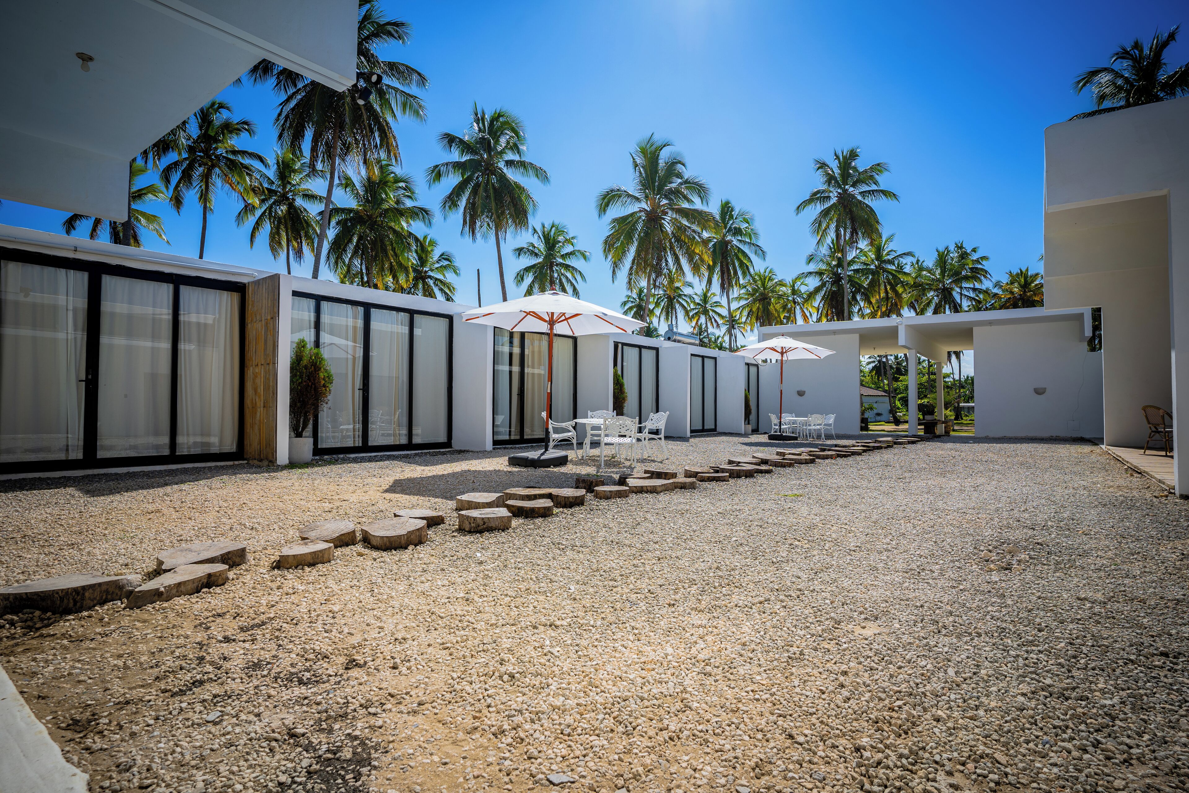 A modern resort with a gravel courtyard, palm trees, and outdoor seating areas.