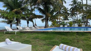 Zona junto a la piscina con sillones de descanso y una piscina, rodeada de palmeras y vista al océano.