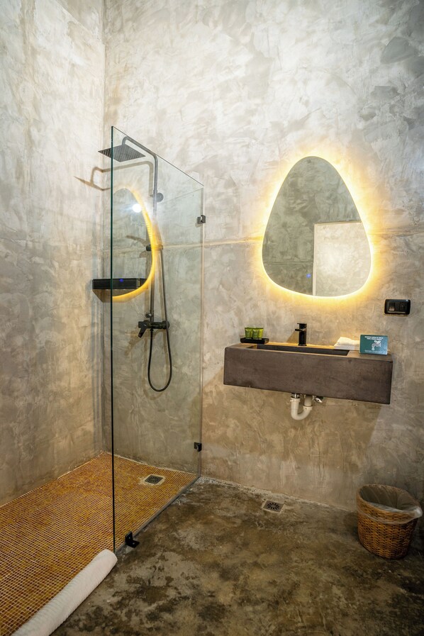 Un baño moderno con ducha envuelta en vidrio, tocador con espejo y pared con textura.