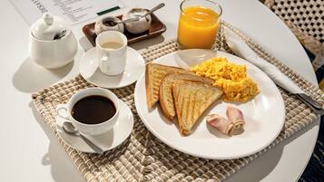 Un desayuno con huevos revueltos, tostadas y jamón, acompañado de café y jugo de naranja.