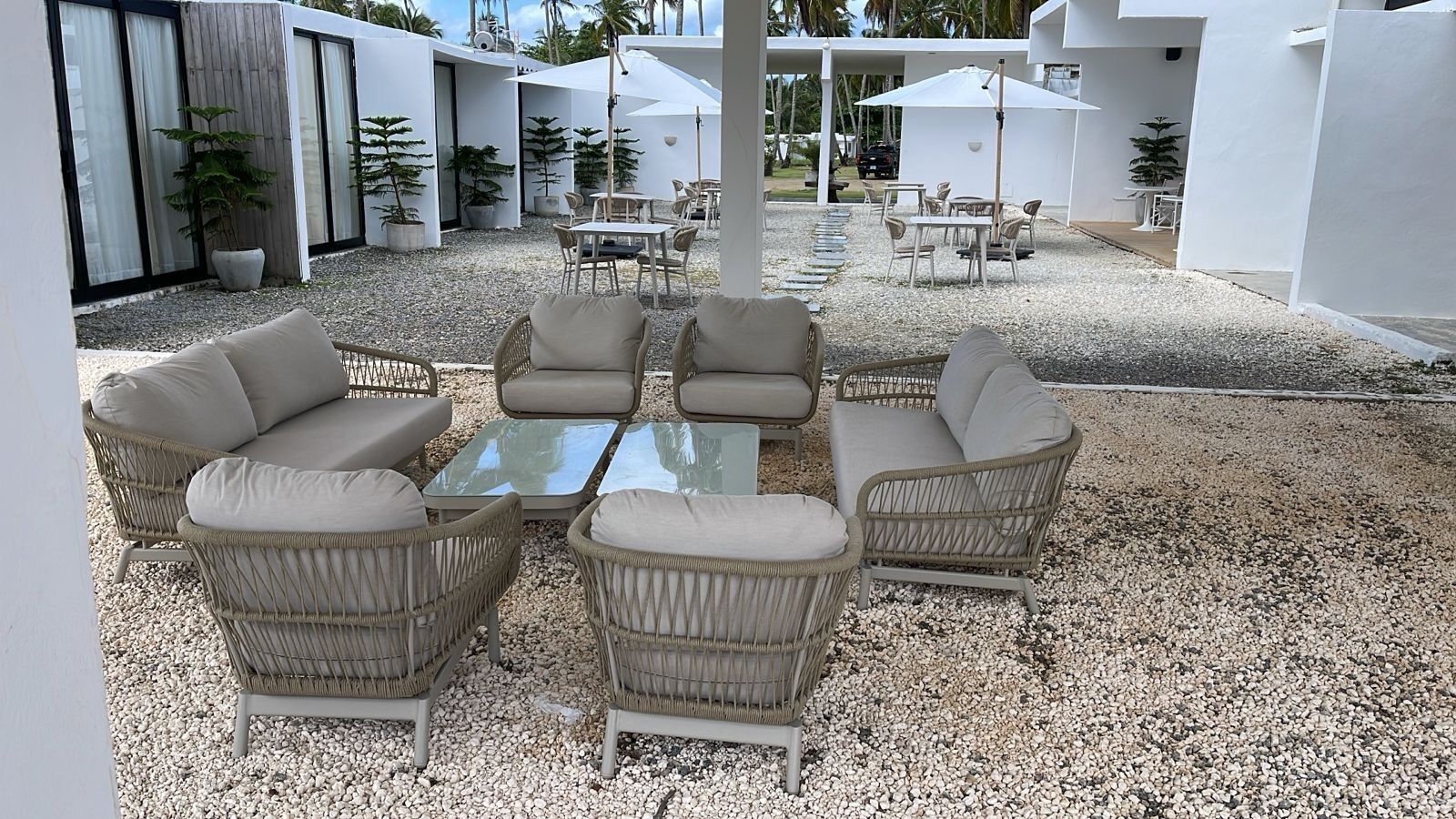 Eine Terrasse mit Korbmöbeln, einem Glastisch und Sonnenschirmen.