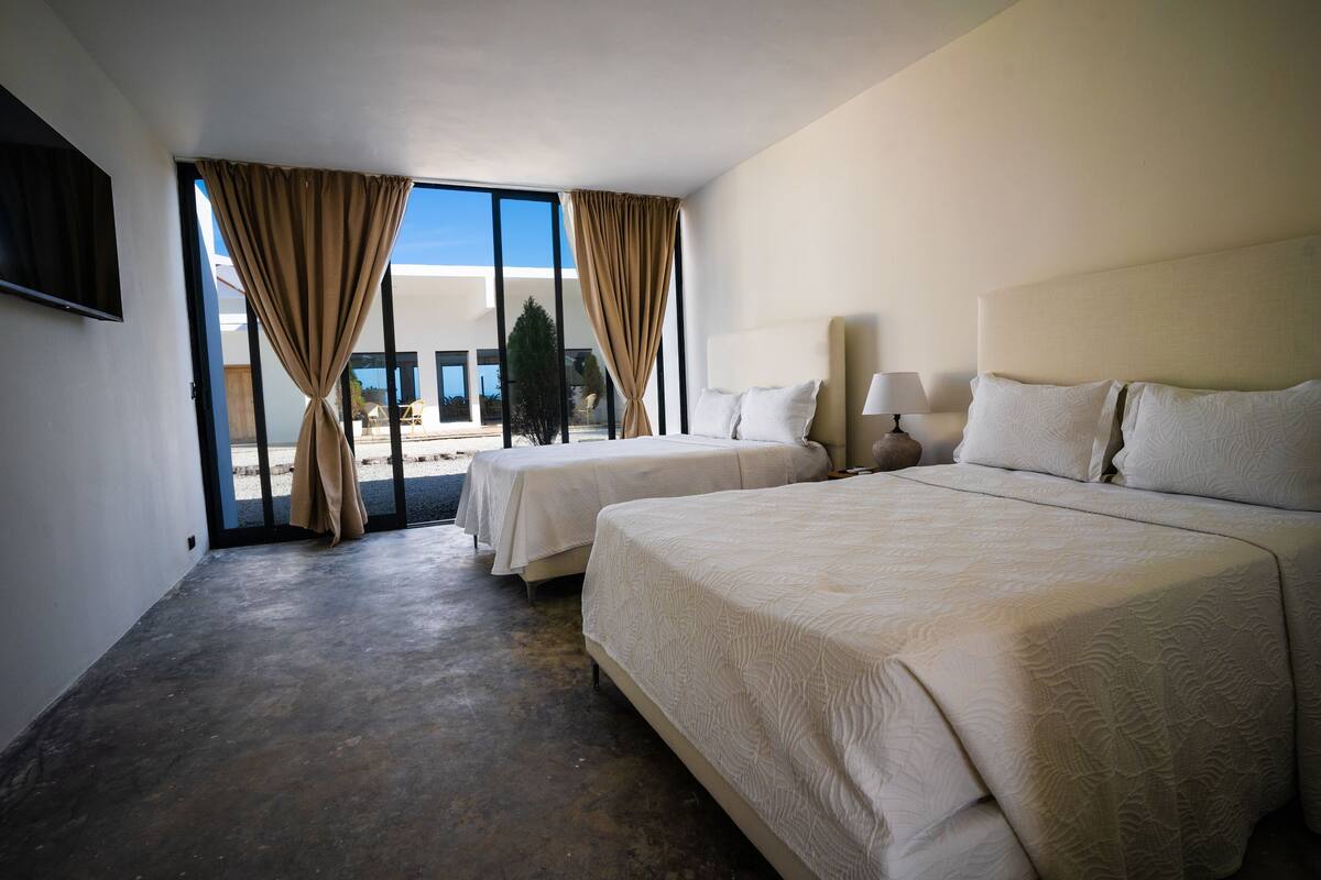 Habitación de hotel con dos camas, un ventanal con cortinas, un televisor de pantalla plana y una lámpara.