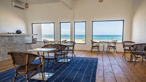 Ein Essbereich am Strand mit Korbstühlen, einem Tisch und großen Fenstern mit Blick auf das Meer.