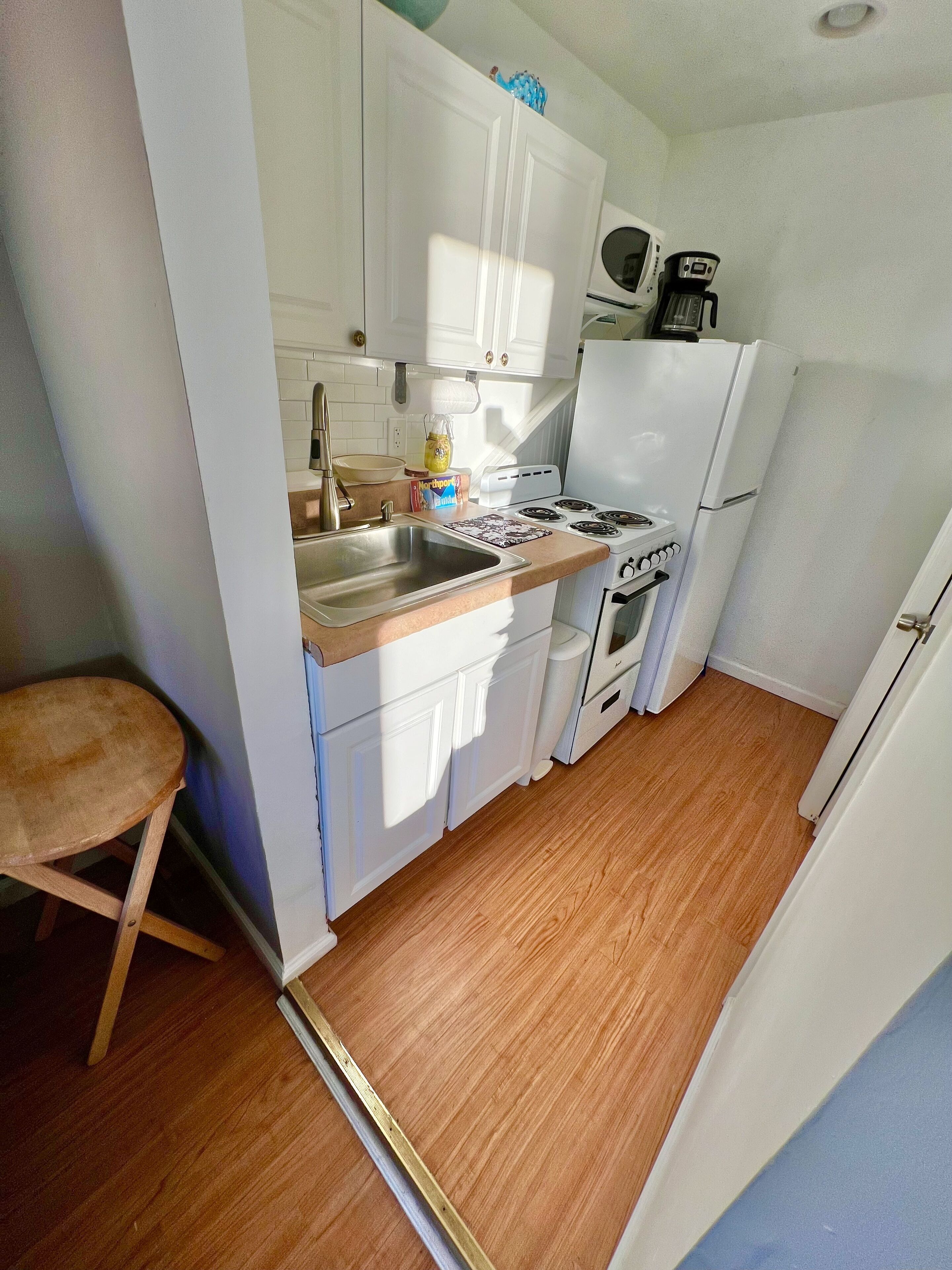 A compact kitchen with white cabinets, a stove, a sink, and a refrigerator.