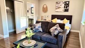 A modern living room with a dark grey sofa, a coffee table, and a bed with yellow pillows.