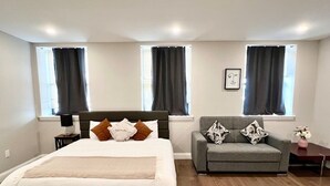 A bedroom with a bed, a sofa, and two windows with curtains. - 306 Deluxe King suite in the center city (Philadelphia)