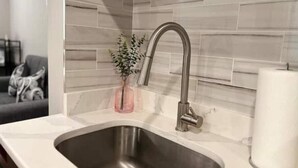 A modern kitchen with a stainless steel sink, a vase with a plant, and a marble backsplash. - 306 Deluxe King suite in the center city (Philadelphia)