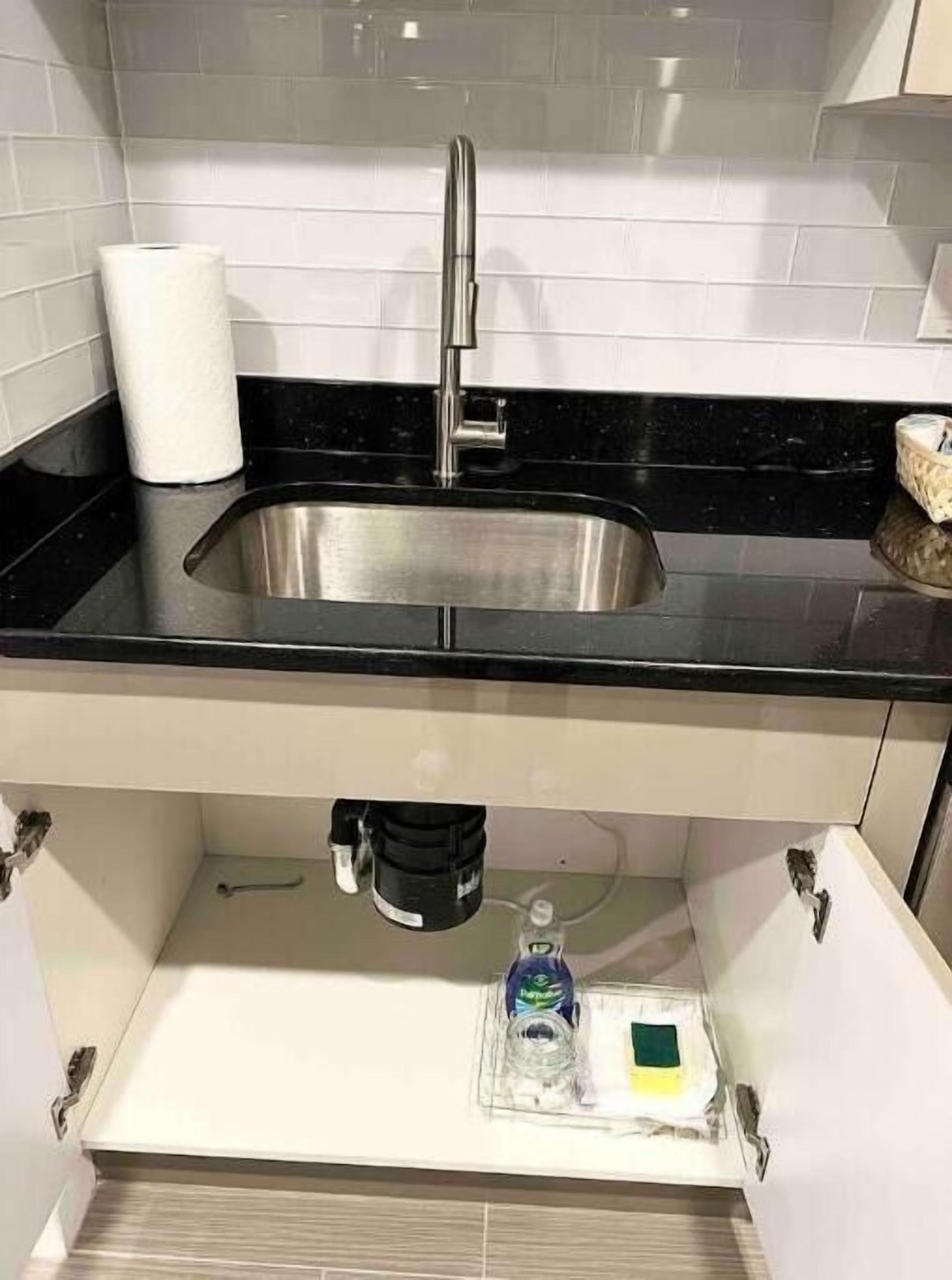 Una cocina moderna con un lavamanos de acero inoxidable, encimera negra y salpicadero de azulejos blancos.