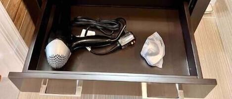 A bathroom vanity with a white sink, dark wooden cabinets, and a drawer containing a hairdryer, a power cord, and a tissue.