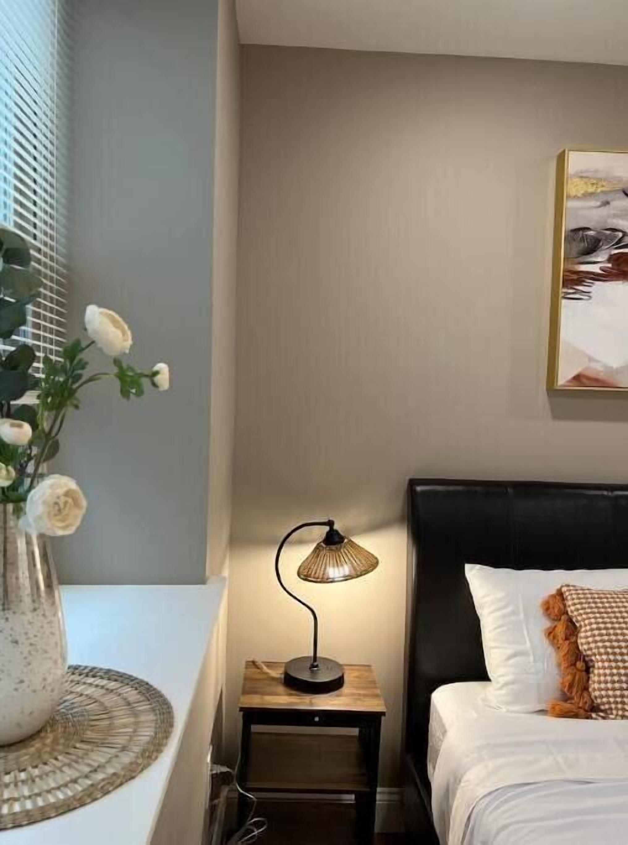 Une chambre à coucher avec un lit, une table de chevet avec une lampe, un vase de fleurs et un tableau au mur.