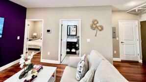 A modern living room with a sofa, coffee table, and decorative items. A television is mounted on the wall, and there is a door leading to another room. - 504 Luexy 1BDR apt in center city (Philadelphia)