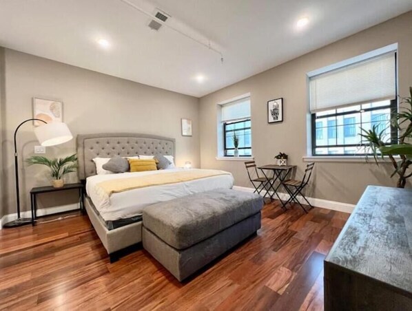A bedroom with a bed, bedside table, lamp, and a small seating area with a chair and table. - 508 Urban Lifestyle king bed APT in Center city (Philadelphia)
