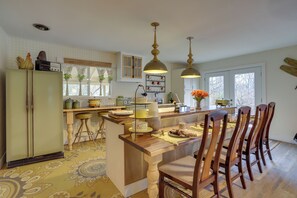 Una cocina con una isla central, sillas de madera, luces colgantes y un refrigerador.