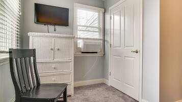 A room with a television mounted on the wall, a window with blinds, a white door, and a chair.