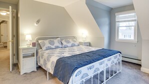 Un dormitorio con una cama, mesitas de noche, una ventana y una puerta.