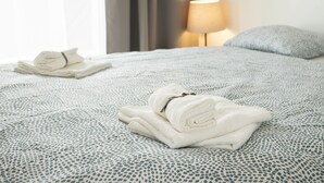 A neatly made bed with a patterned bedspread, a folded towel, and a bedside lamp. - Lomená Apartment
 (Košický kraj)