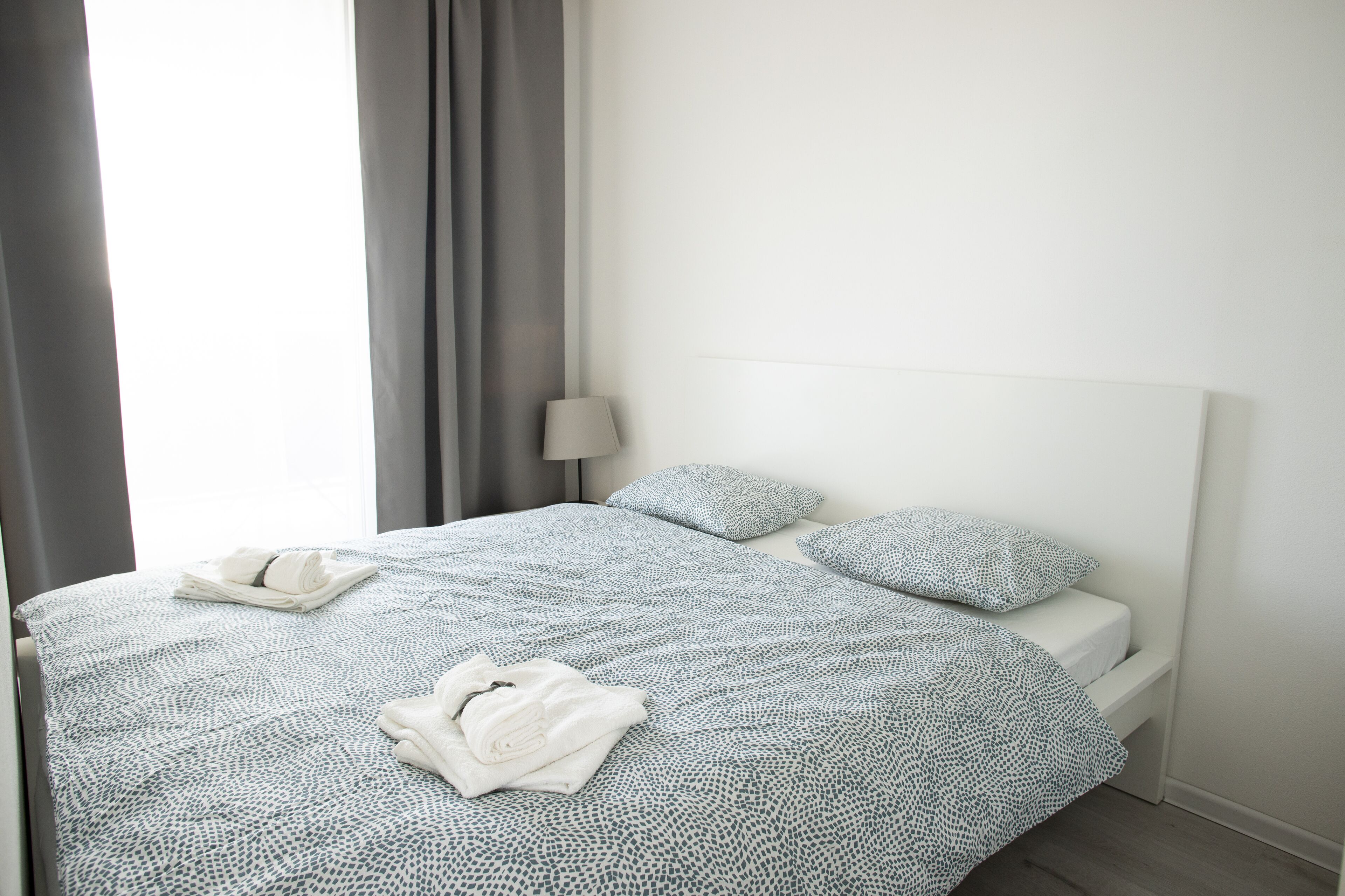 Ein ordentlich bezogenes Bett mit einem gemusterten Überwurf, Kissen und gefalteten Handtüchern.