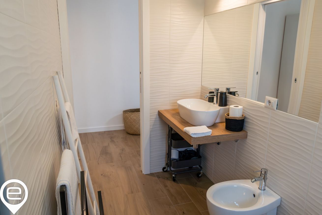 A modern bathroom with a wooden floor, a white sink, a mirror, and a toilet.