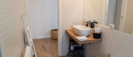 A modern bathroom with a wooden floor, a white sink, a mirror, and a toilet.