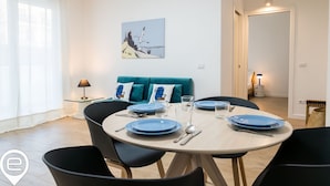 Un comedor con una mesa redonda preparada para cuatro personas, un sofá color turquesa y un cuadro en la pared.