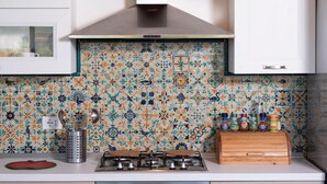 Une cuisine équipée d’une cuisinière à gaz, d’une hotte en acier inoxydable et d’un dosseret carrelé orné d’un motif floral.