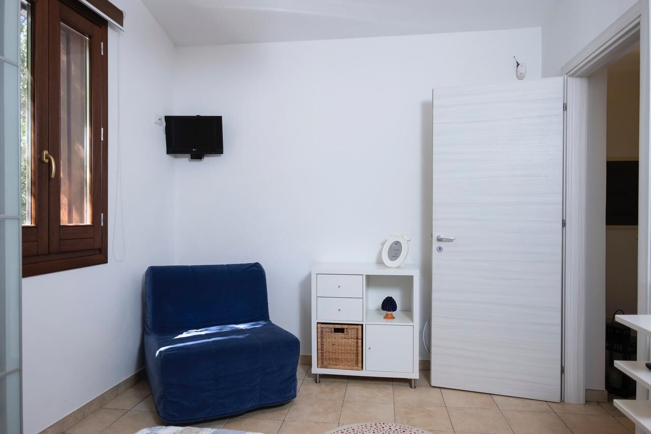 A small, well-lit room with a blue sofa, a white cabinet with a basket, a closed door, and a mounted television.