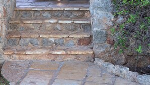 Un escalier en pierre menant à une porte, le tout entouré d’un mur de pierre et de quelques plantes.