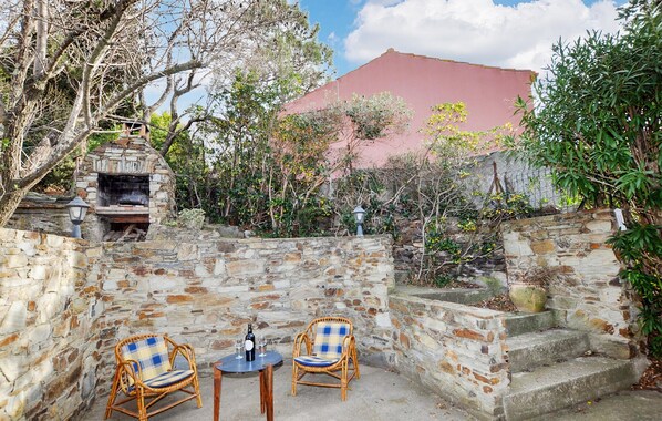 An outdoor patio with stone walls, a stone fireplace, and two wicker chairs with a bottle of wine on a table. - Amazing home in Collioure with house a panoramic view (Collioure)
