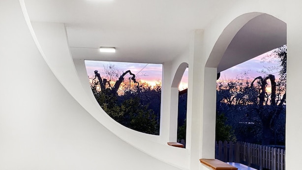 Un interior moderno con paredes blancas curvas y vistas a un atardecer a través de una ventana.