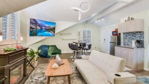 Ein modernes Wohnzimmer mit Sofa, Couchtisch und Fernseher. Es gibt eine Küchenzeile mit Schränken und einer Mikrowelle.