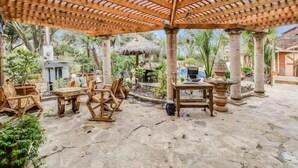 Eine Terrasse im Freien mit Holzmöbeln, einem Reetdach und Steinböden.