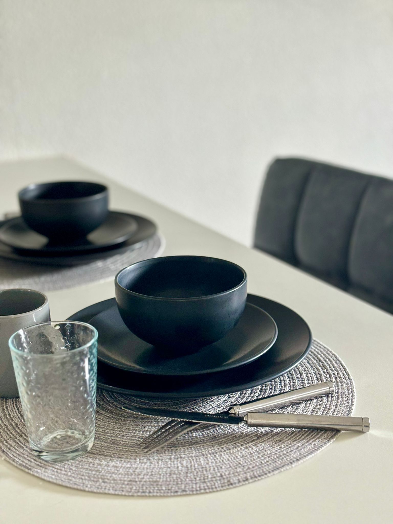 Una mesa con platos y tazones negros, un vaso y un tenedor de acero inoxidable sobre un camino de mesa tejido.