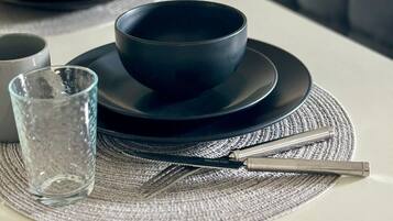 Una mesa con platos y tazones negros, un vaso y un tenedor de acero inoxidable sobre un camino de mesa tejido.