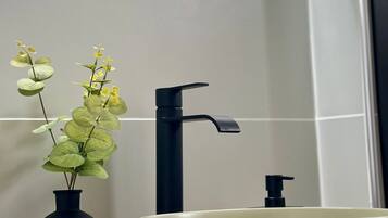 Een moderne badkamer met een rond wastafel, een zwarte kraan en een zwarte vaas met groene bladeren.