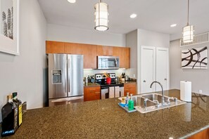 Una cocina moderna con electrodomésticos de acero inoxidable, armarios de madera, encimeras de granito e iluminación colgante.