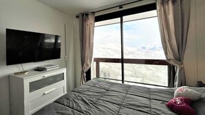 Quarto com cama, televisão em uma cômoda e janela com cortinas.