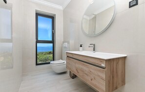 Een moderne badkamer met toilet, wastafel met spiegel en uitzicht op zee.