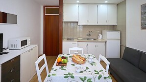 A compact kitchen with white cabinets, a microwave, a sink, and a refrigerator. There's a dining table with a fruit platter and a white tablecloth. - Beachfront Apartment with Wifi and Easy Access to Attractions (Lloret de Mar)