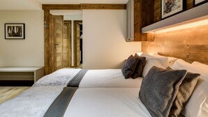 A bedroom with a wooden headboard, a bed with white bedding, a fluffy white rug, and a bench. - Spacious chalet in resort center, 10 people, pets allowed (La Plagne 1800)