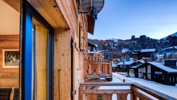 A wooden building with a balcony overlooking a snowy village. - Spacious chalet in resort center, 10 people, pets allowed (La Plagne 1800)