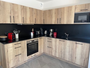 Una cocina moderna con armarios de madera, encimera negra y electrodomésticos de acero inoxidable, incluyendo microondas, cafetera y tostadora.