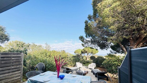 Eine Terrassensitzgruppe im Freien mit Tisch für sechs Personen, umgeben von Stühlen und Blick auf einen Garten mit Bäumen und Sträuchern.