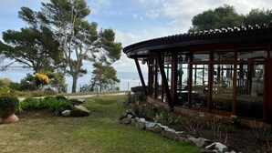 A coastal building with a glass facade, a stone pathway, and a view of the sea. - Apartment 'Eden Mar Calonge Girona' with Sea View, Shared Pool and Air Conditioning (Calonge)