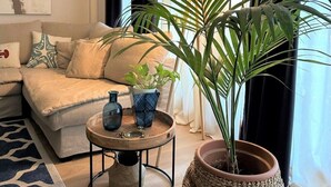 A living room with a sofa, a coffee table with decorative items, a large potted plant, and a painting on the wall. - Apartment 'Eden Mar Calonge Girona' with Sea View, Shared Pool and Air Conditioning (Calonge)