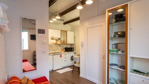A compact living space with a kitchenette, a sofa with striped cushions, a dining area, and a glass-fronted cabinet with dishes. - Studio Apartment "Casa Loredana" with Private Terrace & Wi-Fi (Venezia)