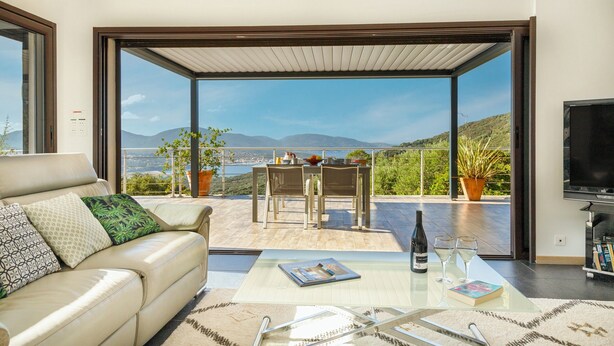 A modern living room with a sofa, a coffee table, a TV, and a balcony with a table and chairs.