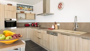 A modern kitchen with wooden cabinets, a stainless steel sink, and a bowl of fruit on the counter.