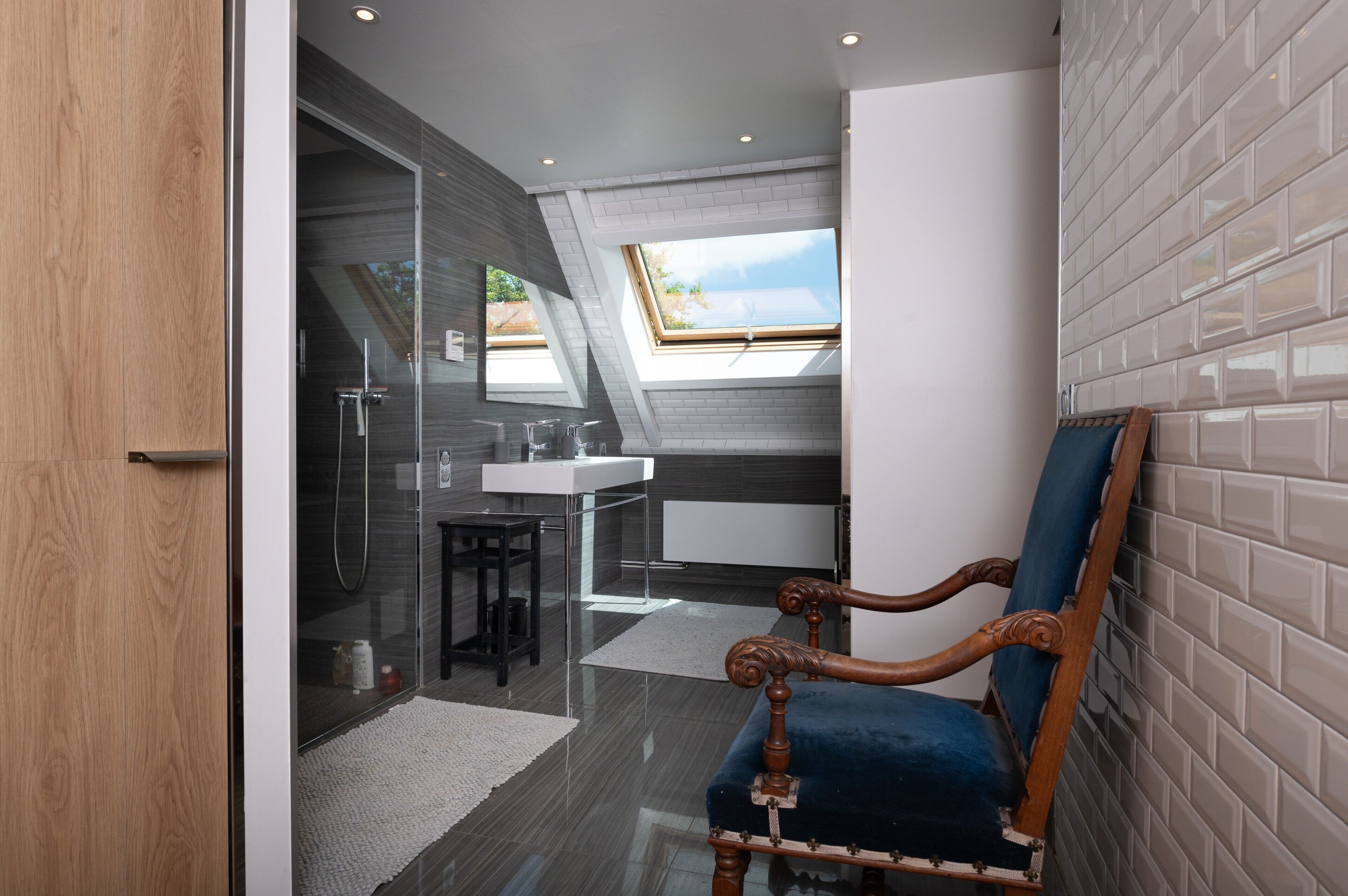 Ein modernes Badezimmer mit Dachfenster, Duschkabine aus Glas und einem Holzstuhl.